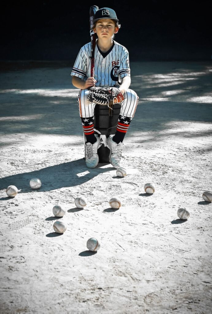 Little League Baseball player inuniform posing on the bucket of baseballs, holding his bat over his right shoulder.
