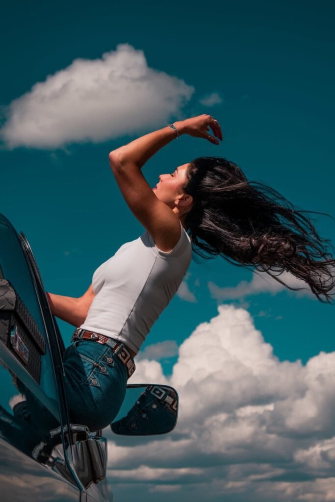Young lady with long hair sitting on the door of a restored Chevy pickup with blue sky in the background.