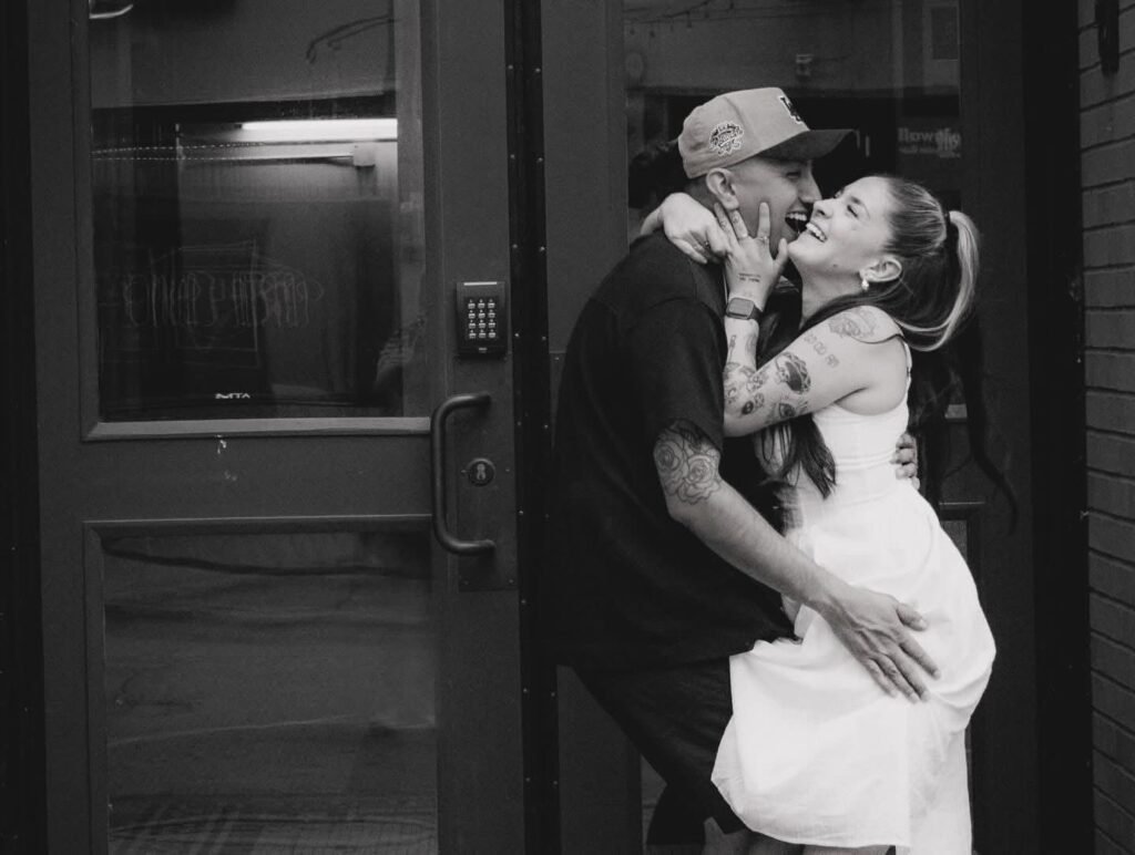 Man and woman embracing, laughing in a doorway.