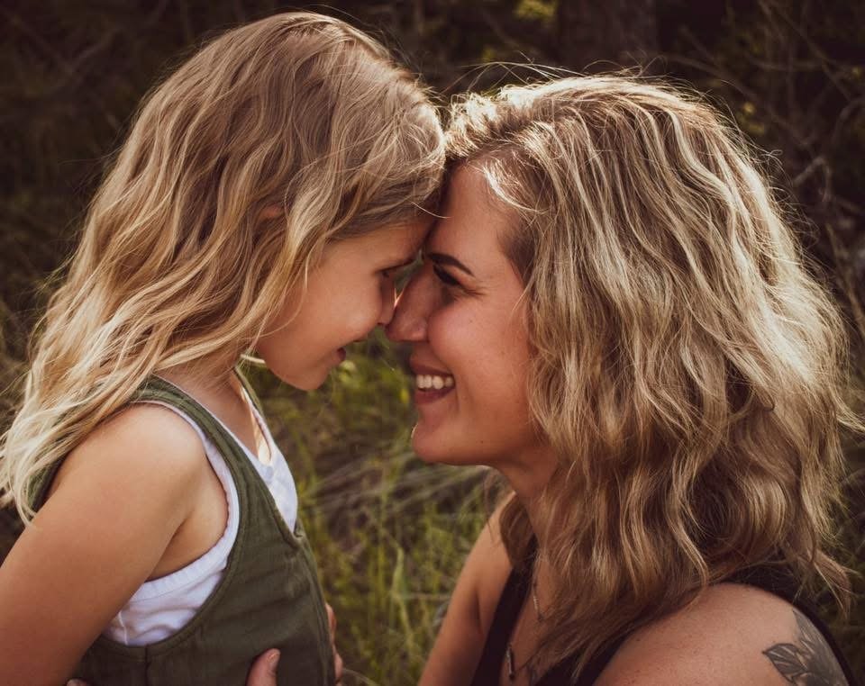 A young mother and her daughter press their foreheads and noses together in a light-hearted moment.