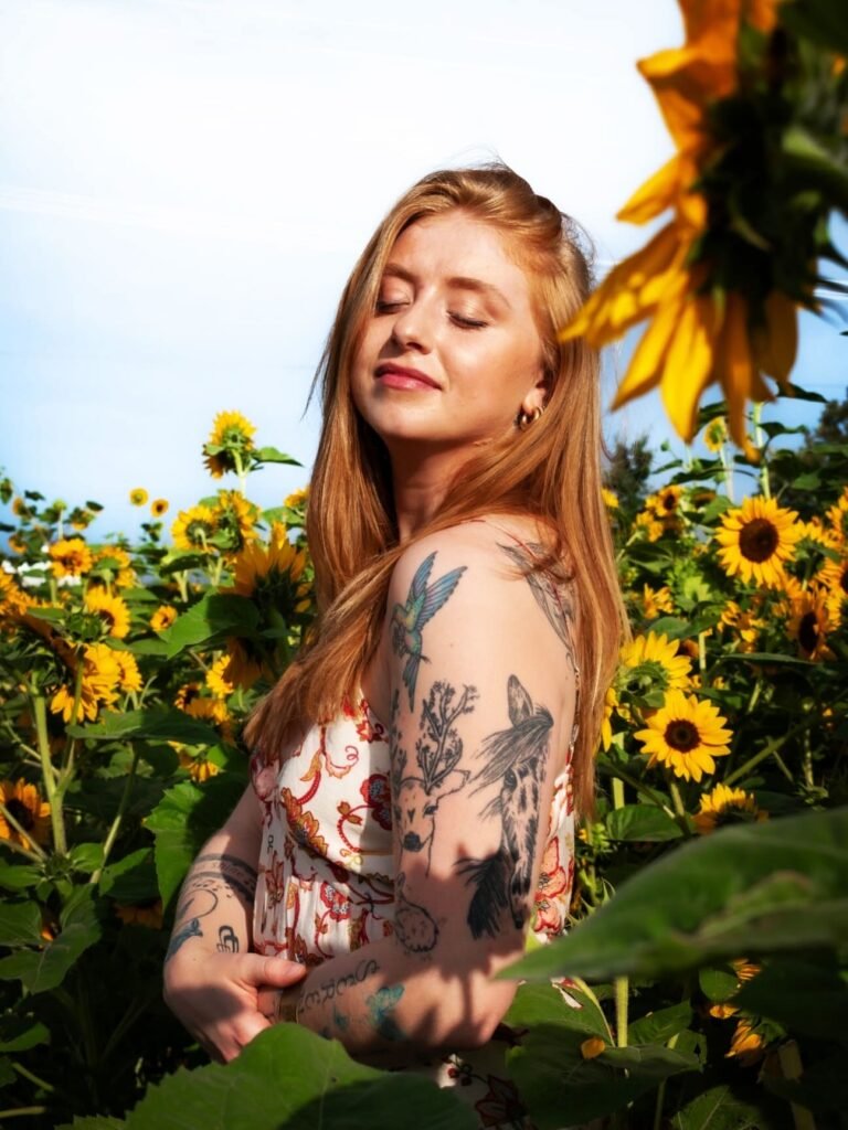 A young woman with tattoos on her arm in a field of sunflowers.