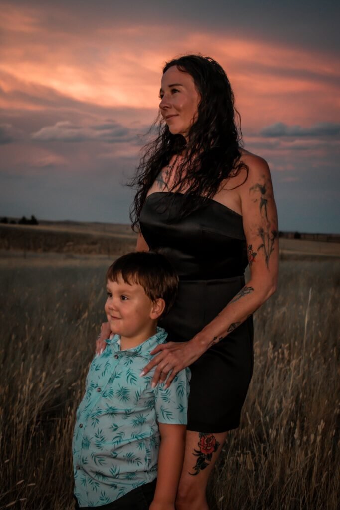 A woman and her little boy stand for a portrait outside at sundown.