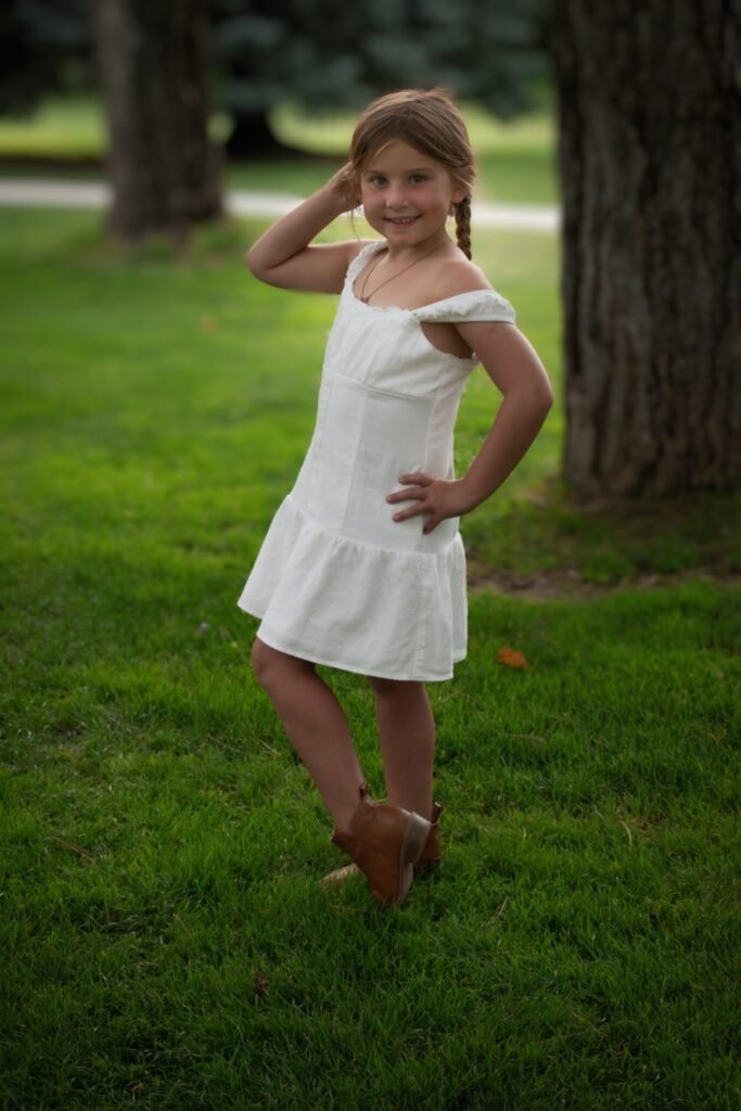 A young girl in a white dress poses for the photographer in a park.