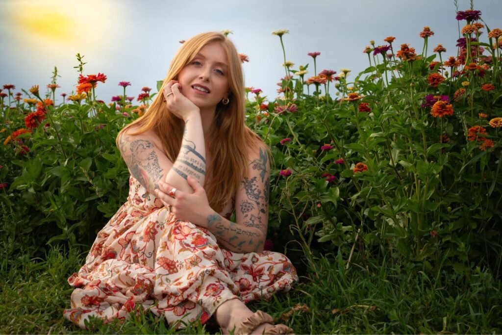 A young woman in a sundress sitting in front of a bed of blooming zinnias.