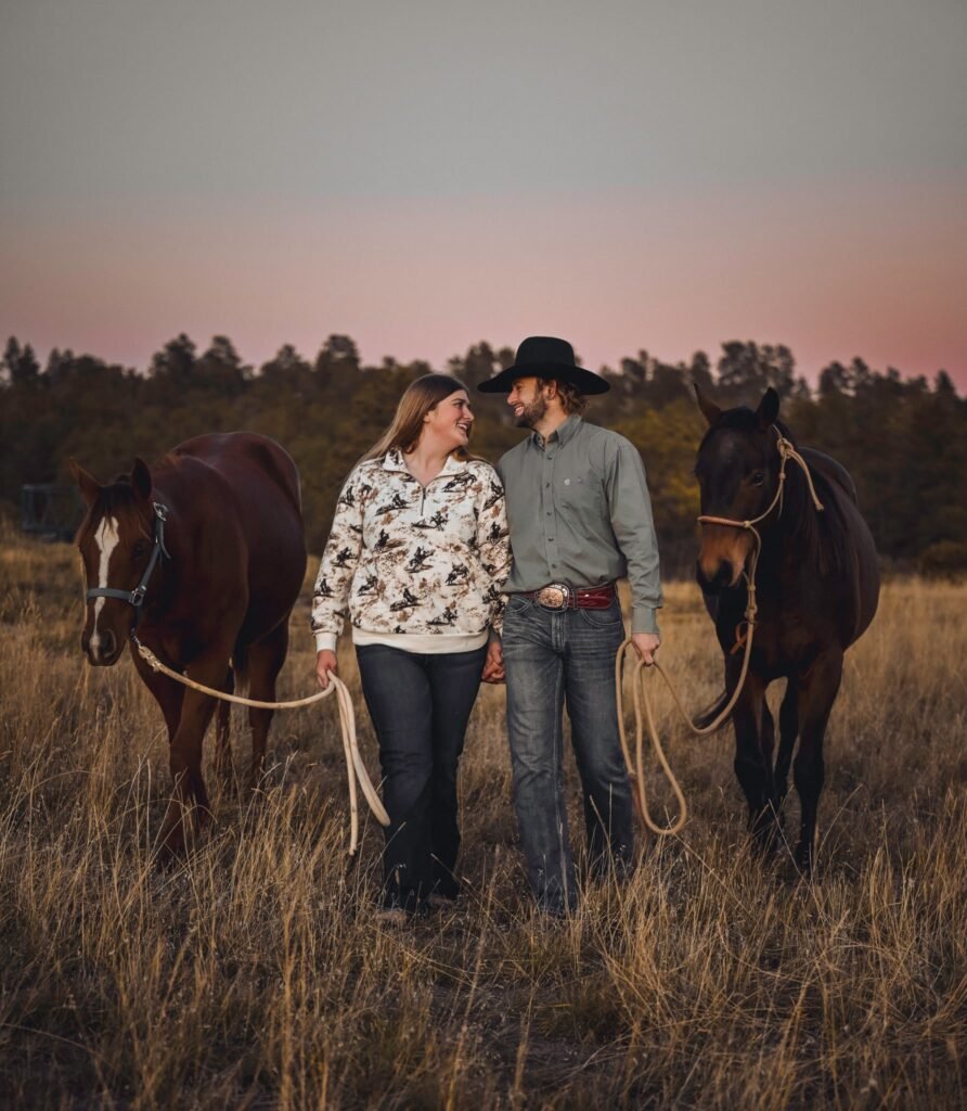 A young man and woman leading two horses in a field.