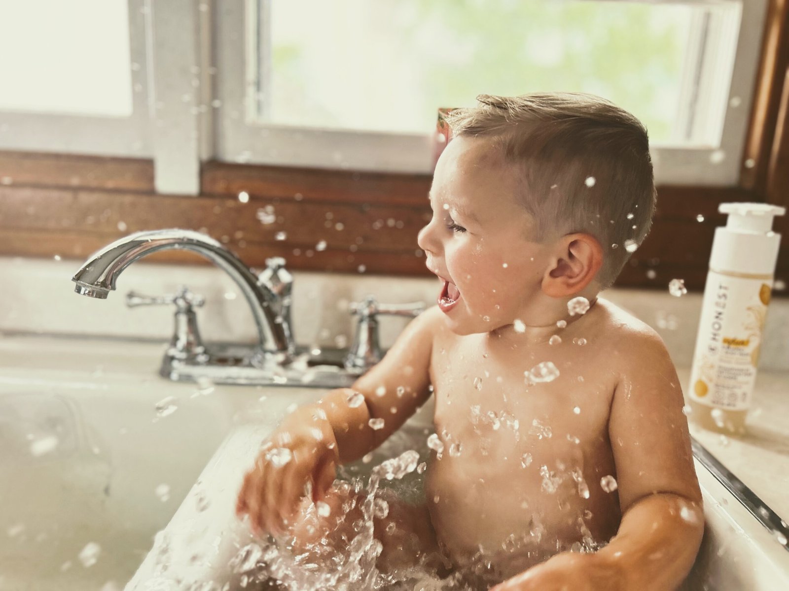 Toddler taking a bath in the kitchen sink.