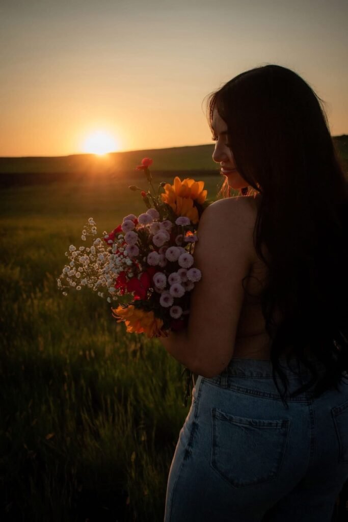 Young woman with colorful bouquet in a field of grass at sundown.