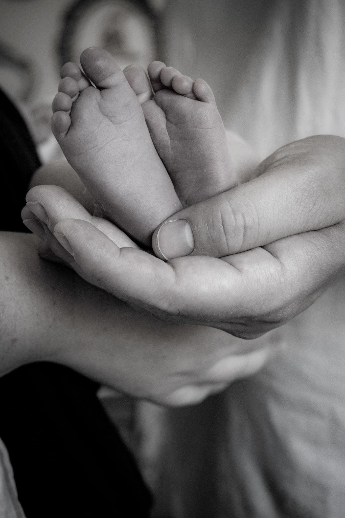 Black and white image of a newborn baby's feet cradled in her father's hand.