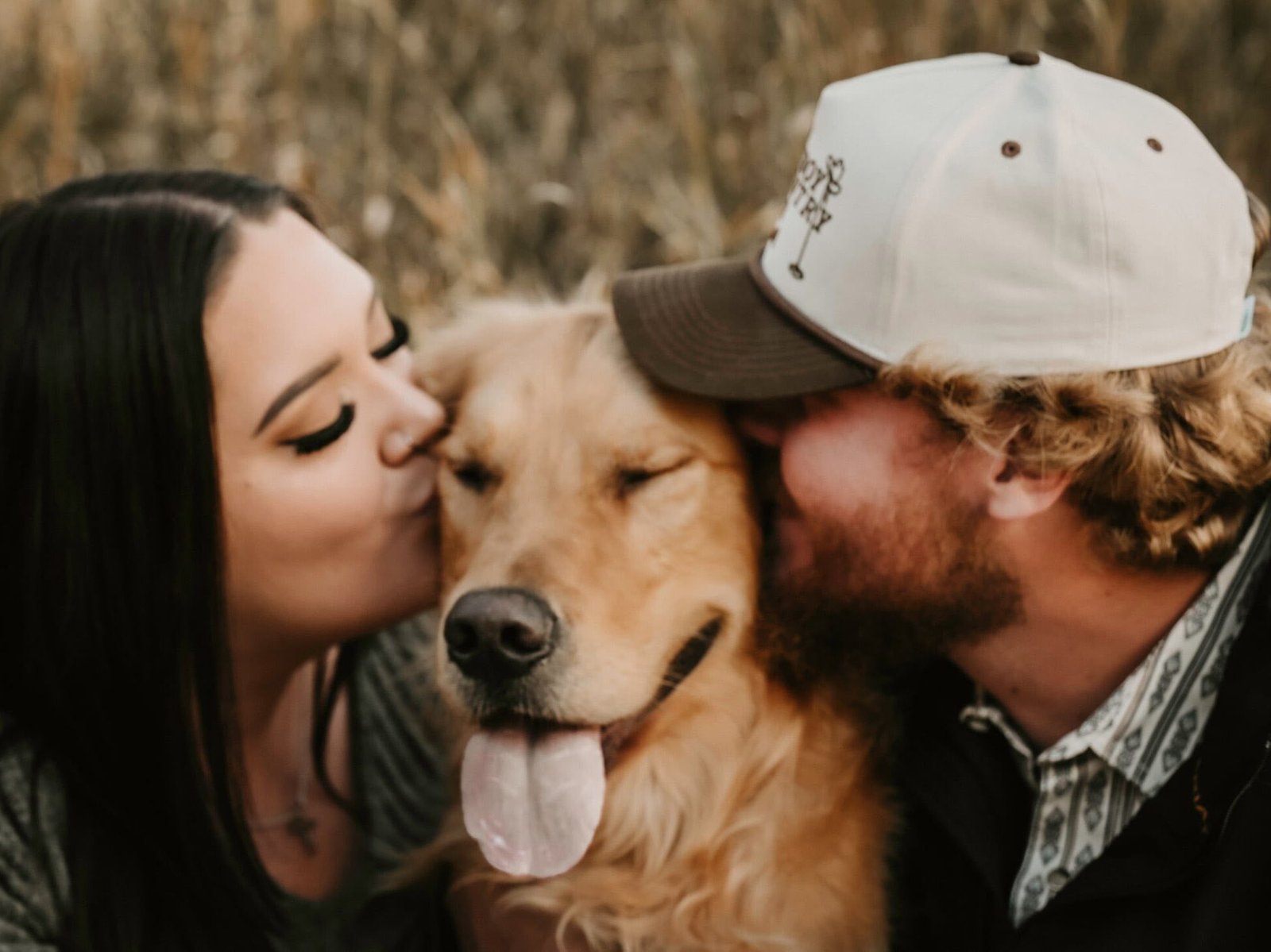 A young man and woman each kissing a Golden Retriever.